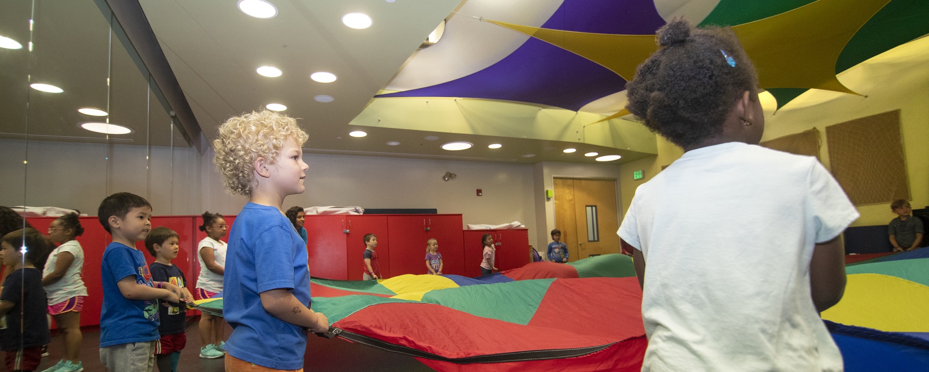 Young children standing in a circle and holding the edges of a parachute.