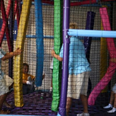 3 boys playing with long, vertical, colorful plastic pool noodles.