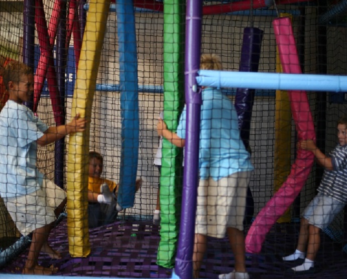 3 boys playing with long, vertical, colorful plastic pool noodles.
