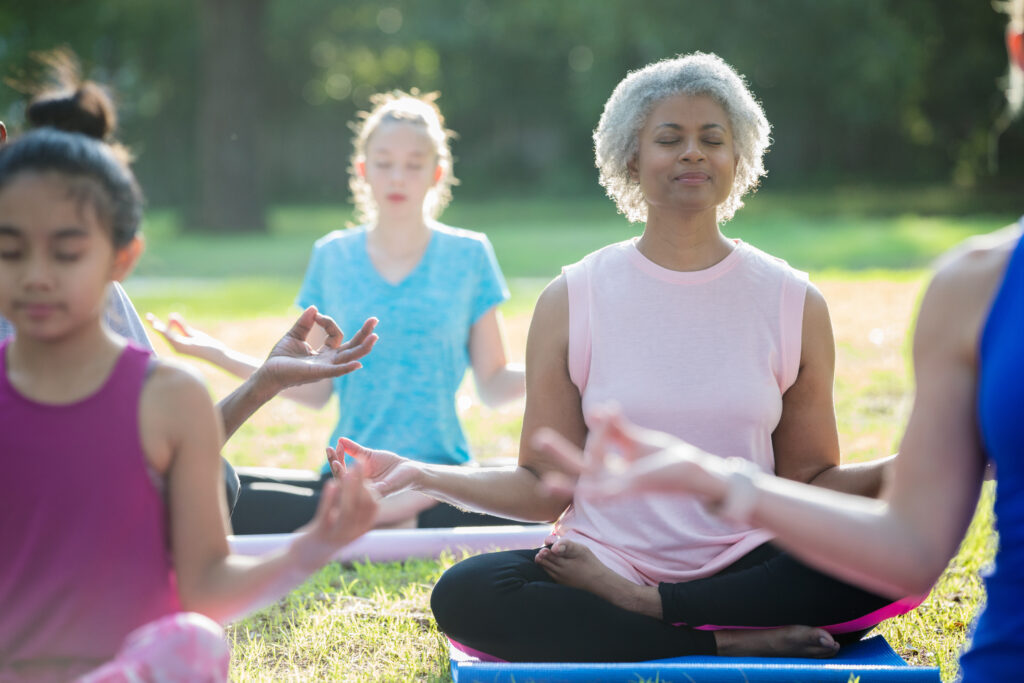 Senior adult African American woman taking outdoor yoga class with diverse group of people outdoors in community park.