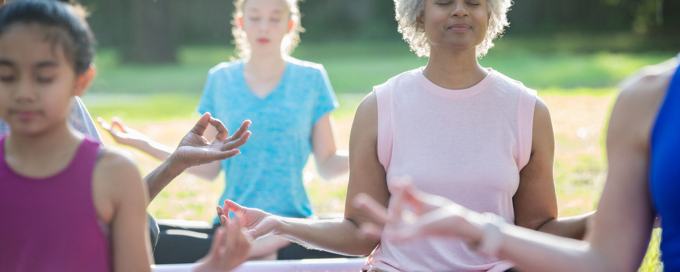 Senior adult African American woman taking outdoor yoga class with diverse group of people outdoors in community park.